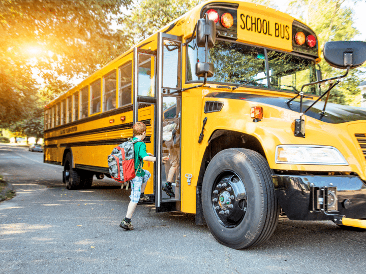 A young student with a backpack boarding a yellow school bus on a sunny day.