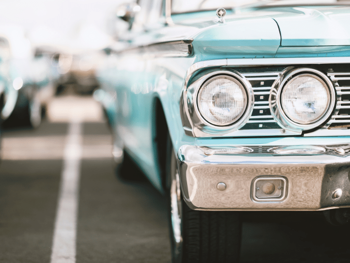 Front view of a vintage turquoise car with chrome detailing and headlights, parked in a lot.