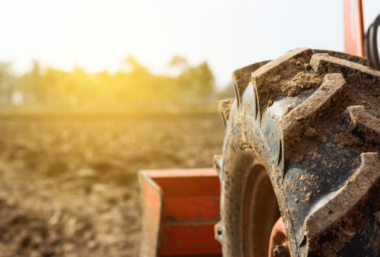 Close-up of a muddy tractor tire in a plowed field with the sun setting in the background.