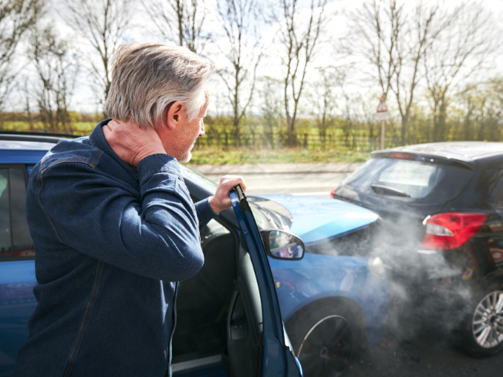 Man, standing with his hand on the back of his neck and looking back at his car and another vehicle involved in a fender bender.