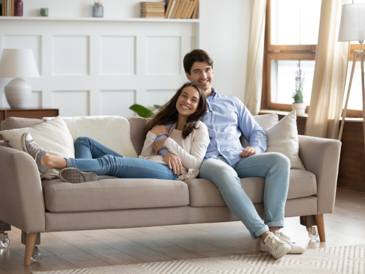 A male-female couple sitting together on a couch, in their rented living space.