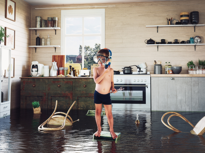 Boy child standing on a box in the middle of his kitchen, wearing a snorkel as water begins to rise around him. Demonstrating a home flood.