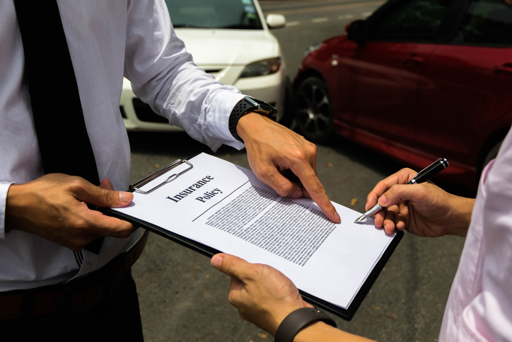 An insurance agent showing a client the details of a car insurance policy and pointing to a section on the document
