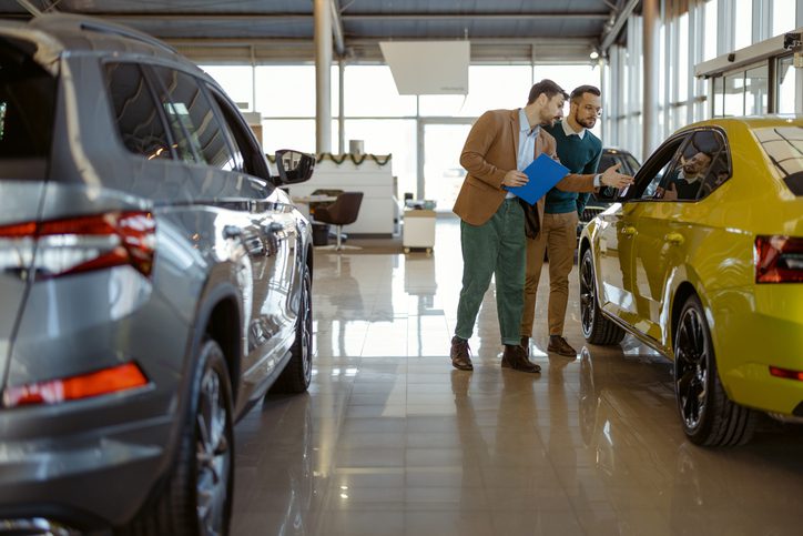 A car insurance agent showing a yellow car to a customer inside a dealership.