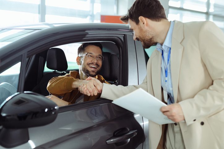 Happy customer shaking hands with a car dealer after financing a vehicle.