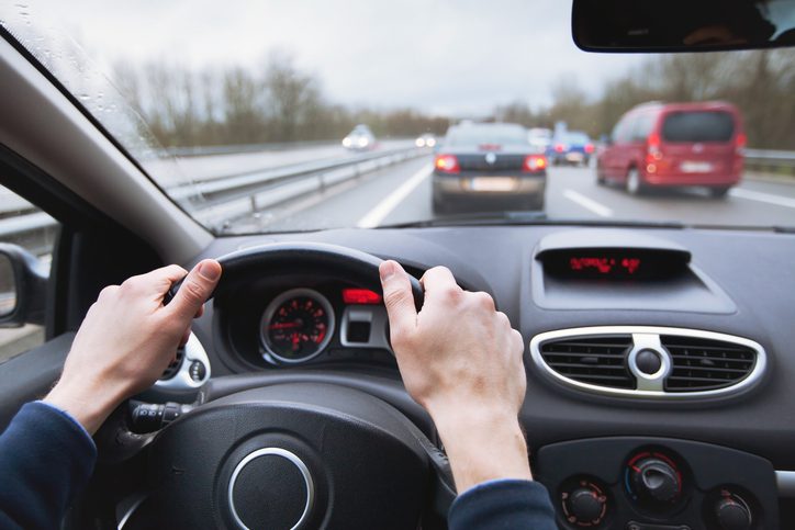 Driver holding a steering wheel on a busy highway in traffic, illustrating driving with g2 license restrictions.