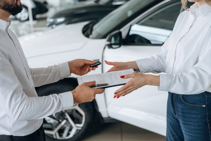 Customer and car dealer discussing documents and car keys, representing the decision between leasing vs financing a car.