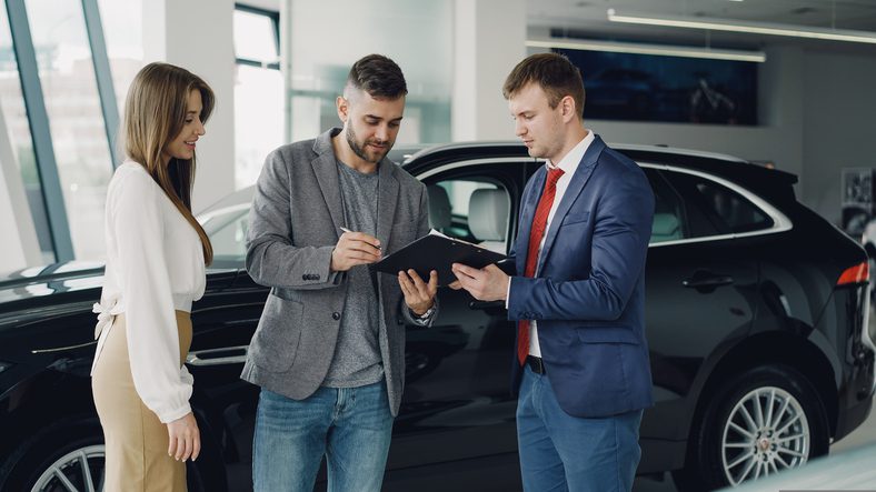 Car dealer assisting a couple with vehicle financing paperwork, representing tax deductions and limits on business car financing costs.