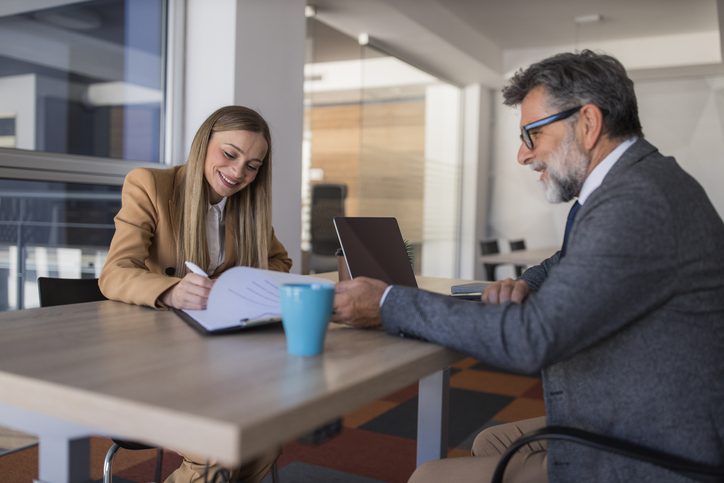 An insurance broker meets with a woman in a modern office to review specific policy limits and exclusions, helping her avoid the “full coverage” trap through detailed explanation.